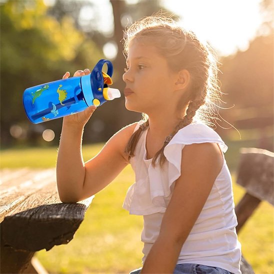 Fillette boit avec gourde enfant bleue au parc