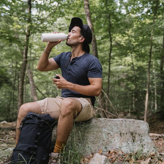 Homme boit avec gourde isotherme dans forêt