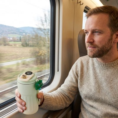Homme voyage en train tient mug isotherme vert